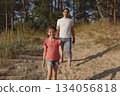 Father and daughter walk one after other along beach sand near forest in summer, lifestyle 134056818