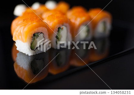 Salmon sushi set. Sushi roll Philadelphia with red fish, salmon, red caviar. Roll with soft avocado and cream cheese under a layer of massago caviar. Classic sushi on a black background. Food. 134058231