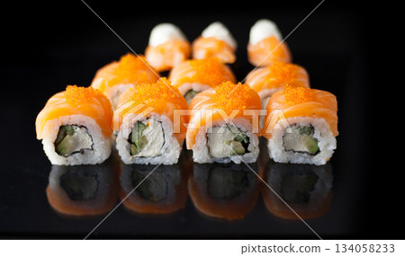 Salmon sushi set. Sushi roll Philadelphia with red fish, salmon, red caviar. Roll with soft avocado and cream cheese under a layer of massago caviar. Classic sushi on a black background. Food. Salmon sushi set. Sushi roll Philadelphia with red fish, salmon, red caviar. Roll with soft avocado and cream cheese under a layer of massago caviar. Classic sushi on a black background. Food. 134058233