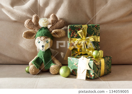 Crocheted Reindeer with Christmas Gift Box and Ornaments on Cozy Holiday Background Crocheted Reindeer with Christmas Gift Box and Ornaments on Cozy Holiday Background 134059005