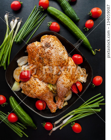 Whole raw chicken marinated with soy sauce and spices added with cherry tomatoes and leek in pan. Whole raw chicken marinated with soy sauce and spices added with cherry tomatoes and leek in pan. 134059087