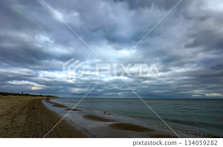 A serene beachscape unfolds under a canopy of cloudy skies, creating a picturesque scene 134059282
