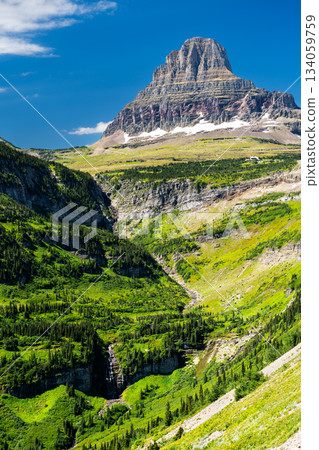 Reynolds Creek flows through green valley below Clements Mountain in Glacier National Park, Montana. Scenic landscape features waterfall and rocky peaks in UNESCO World Heritage site 134059759