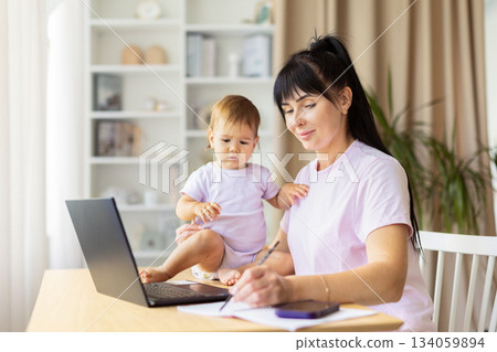 Mother writing notes while her baby sitting nearby on the table Mother writing notes while her baby sitting nearby on the table 134059894