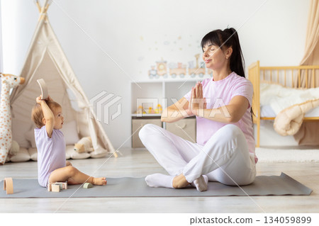 Mother practicing yoga on mat while baby watching and playing with toys 134059899