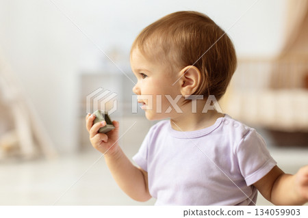 Baby holding small block toy while looking to the side Baby holding small block toy while looking to the side 134059903