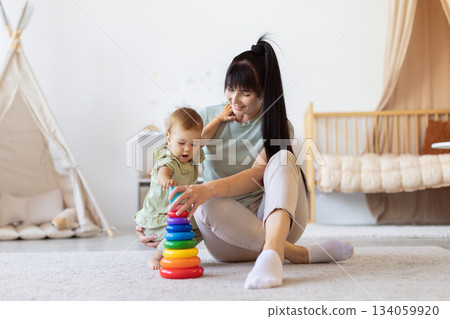 Mother sitting on floor helping her baby play with colorful stacking toys Mother sitting on floor helping her baby play with colorful stacking toys 134059920