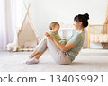 Mother sitting on floor holding her laughing baby on her lap 134059921