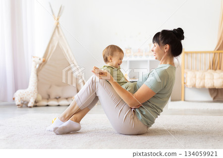 Mother sitting on floor holding her laughing baby on her lap Mother sitting on floor holding her laughing baby on her lap 134059921