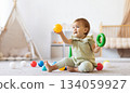 Smiling baby sitting on floor holding colorful ball and ring toy 134059927