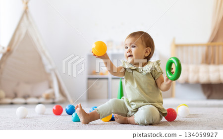 Smiling baby sitting on floor holding colorful ball and ring toy Smiling baby sitting on floor holding colorful ball and ring toy 134059927