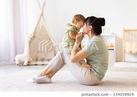Mother sitting on floor holding her baby close as they touch foreheads Mother sitting on floor holding her baby close as they touch foreheads 134059929