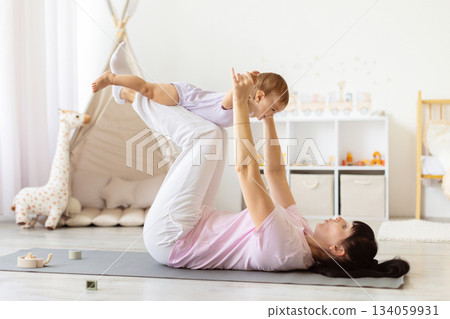 Mother lifting baby above her legs during playful exercise on yoga mat Mother lifting baby above her legs during playful exercise on yoga mat 134059931