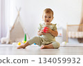 Baby sitting on floor holding red ball looking forward with curiosity 134059932