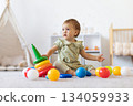 Cute infant baby girl sitting on soft carpet surrounded by colorful toys 134059933