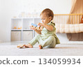 Infant aby sitting on carpet at home playing with wooden toy train 134059934