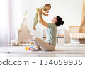 Mother lifting her baby joyfully at home, creating bonding moment 134059935