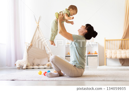 Mother lifting her baby joyfully at home, creating bonding moment Mother lifting her baby joyfully at home, creating bonding moment 134059935