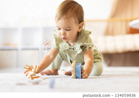 Baby girl kneeling on floor exploring wooden toys with curiosity Baby girl kneeling on floor exploring wooden toys with curiosity 134059936