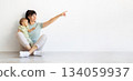 Mother sitting with baby on floor and pointing aside at copy space 134059937