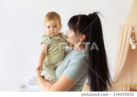 Loving mother holding her infant baby in bright home interior Loving mother holding her infant baby in bright home interior 134059938