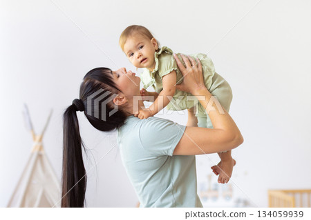 Loving mother lifting her baby playfully, creating joyful bonding moment at home Loving mother lifting her baby playfully, creating joyful bonding moment at home 134059939