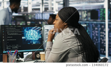 Data center staff member in office using AI deep learning algorithms to analyze datasets. African american woman in server room using artificial intelligence neural networks, camera B 134060172