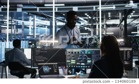 Server hub manager talking with programmer using node tree software to optimize system health. Data center supervisor overseeing IT expert analyzing equipment issues using AI visualization, camera A 134060189