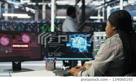 Server farm IT expert responds to security breach alert displayed on computer monitor, working to secure hardware. Data center employee attempts to protect equipment during cyberattack, camera B 134060193