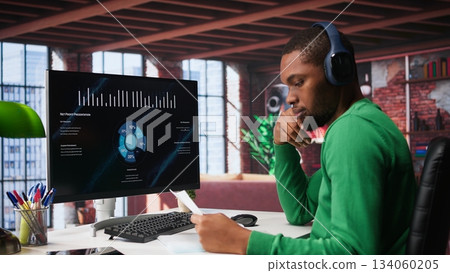 Teleworker in home office watching business conference on PC, looking over statistics charts. African american remote employee in apartment looking at presentation graphs on computer. Camera B. 134060205