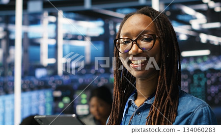 Portrait of smiling server room engineer using device to interpret AI generated data analytics graphs. Happy data center worker using artificial intelligence tool showing system metrics, camera B 134060283