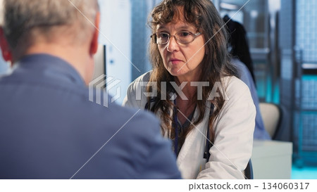 Healthcare specialist sharing medical expertise and reading the MRI scans results with male patient, reviewing x ray reports for the correct diagnostic. Expert discuss treatment plans. Camera B. Healthcare specialist sharing medical expertise and reading the MRI scans results with male patient, reviewing x ray reports for the correct diagnostic. Expert discuss treatment plans. Camera B. 134060317
