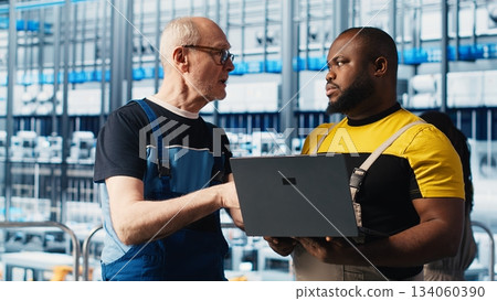 Smart factory senior engineer teaching new trainee to manage robotic arms. Industry 4.0 industrial plant team leader and intern controlling automated machinery, ensuring workflow continuity, camera A 134060390