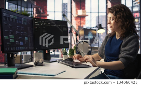 IT specialist at workstation programming on monitor and writing lines of code, using development tools and a terminal window interface. Woman debugging software before deadline. Camera A. IT specialist at workstation programming on monitor and writing lines of code, using development tools and a terminal window interface. Woman debugging software before deadline. Camera A. 134060423