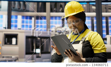 Woman working in solar panels plant uses tablet to oversee machinery systems. African american photovoltaics plant employee uses software on device to maintain operations, camera B Woman working in solar panels plant uses tablet to oversee machinery systems. African american photovoltaics plant employee uses software on device to maintain operations, camera B 134060711