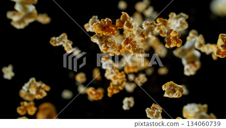 Dynamic macro shot of flying popcorn pieces against a black background. Crisp detail and motion captured in a dramatic, high contrast composition. Perfect for advertising or creative design. 134060739