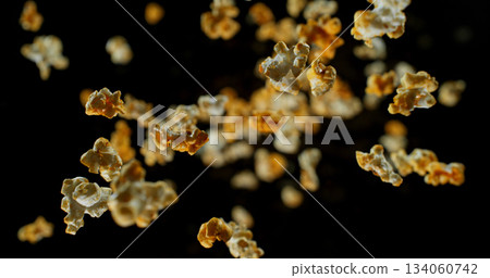 Dynamic macro shot of flying popcorn pieces against a black background. Crisp detail and motion captured in a dramatic, high contrast composition. Perfect for advertising or creative design. Dynamic macro shot of flying popcorn pieces against a black background. Crisp detail and motion captured in a dramatic, high contrast composition. Perfect for advertising or creative design. 134060742