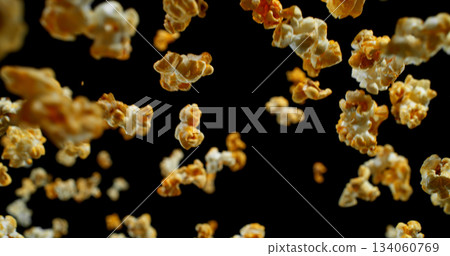 Dynamic macro shot of flying popcorn pieces against a black background. Crisp detail and motion captured in a dramatic, high-contrast composition. Perfect for advertising or creative design. 134060769