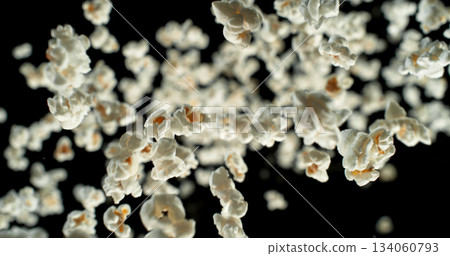 Dynamic macro shot of flying popcorn pieces against a black background. Crisp detail and motion captured in a dramatic, high contrast composition. Perfect for advertising or creative design. Dynamic macro shot of flying popcorn pieces against a black background. Crisp detail and motion captured in a dramatic, high contrast composition. Perfect for advertising or creative design. 134060793