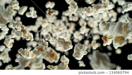 Dynamic macro shot of flying popcorn pieces against a black background. Crisp detail and motion captured in a dramatic, high contrast composition. Perfect for advertising or creative design. Dynamic macro shot of flying popcorn pieces against a black background. Crisp detail and motion captured in a dramatic, high contrast composition. Perfect for advertising or creative design. 134060794