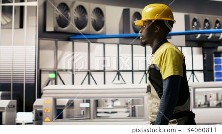 Engineer walking in smart solar manufacturing facility, using toolbox to calibrate high tech machinery. African american man troubleshooting photovoltaic assembly equipment, camera B 134060811