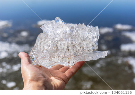 Hand holding clear ice piece over shimmering water surface 134061136