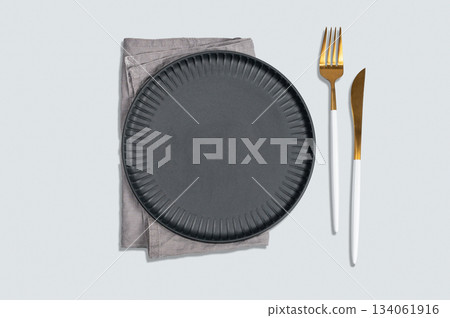 A black textured plate with a fork, knife, and linen napkin on a light background. 134061916