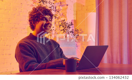 Smiling man working on laptop in warm cozy room Smiling man working on laptop in warm cozy room 134062432