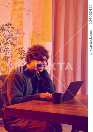 Man working on laptop and drinking coffee in warm evening office. Man working on laptop and drinking coffee in warm evening office. 134062433