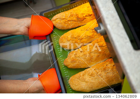 Homemade bread on a baking sheet is taken out of the oven. Long loaf, baguette at home in the kitchen. Bakery products. Cook at home. Homemade bread on a baking sheet is taken out of the oven. Long loaf, baguette at home in the kitchen. Bakery products. Cook at home. 134062809