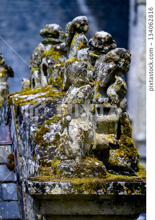 A fragment of an ancient miniature stone sculpture of a knight in armor and holding a sword, covered in moss, blemishes, and age spots. Color, vertical photo. 134062816