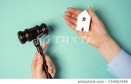 A woman hand holds a wooden house and a judges gavel, symbolizing real estate legal decisions, property inheritance disputes, and the establishment of ownership rights. A woman hand holds a wooden house and a judges gavel, symbolizing real estate legal decisions, property inheritance disputes, and the establishment of ownership rights. 134062896