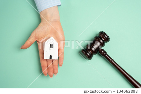A woman hand holds a wooden house and a judges gavel, symbolizing real estate legal decisions, property inheritance disputes, and the establishment of ownership rights. 134062898