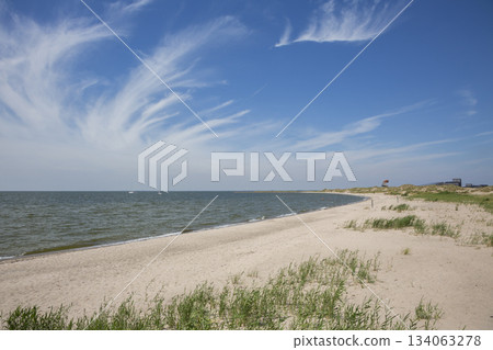 Visit to Marker Wadden beach in The Netherlands during a sunny day by the water with boats in the distance and sandy shore alongside grass Visit to Marker Wadden beach in The Netherlands during a sunny day by the water with boats in the distance and sandy shore alongside grass 134063278